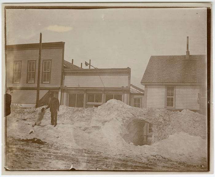 “A man and dog outside the remains of a snow tunnel on Main Street, Breckenridge during the Big Snow of 1899”